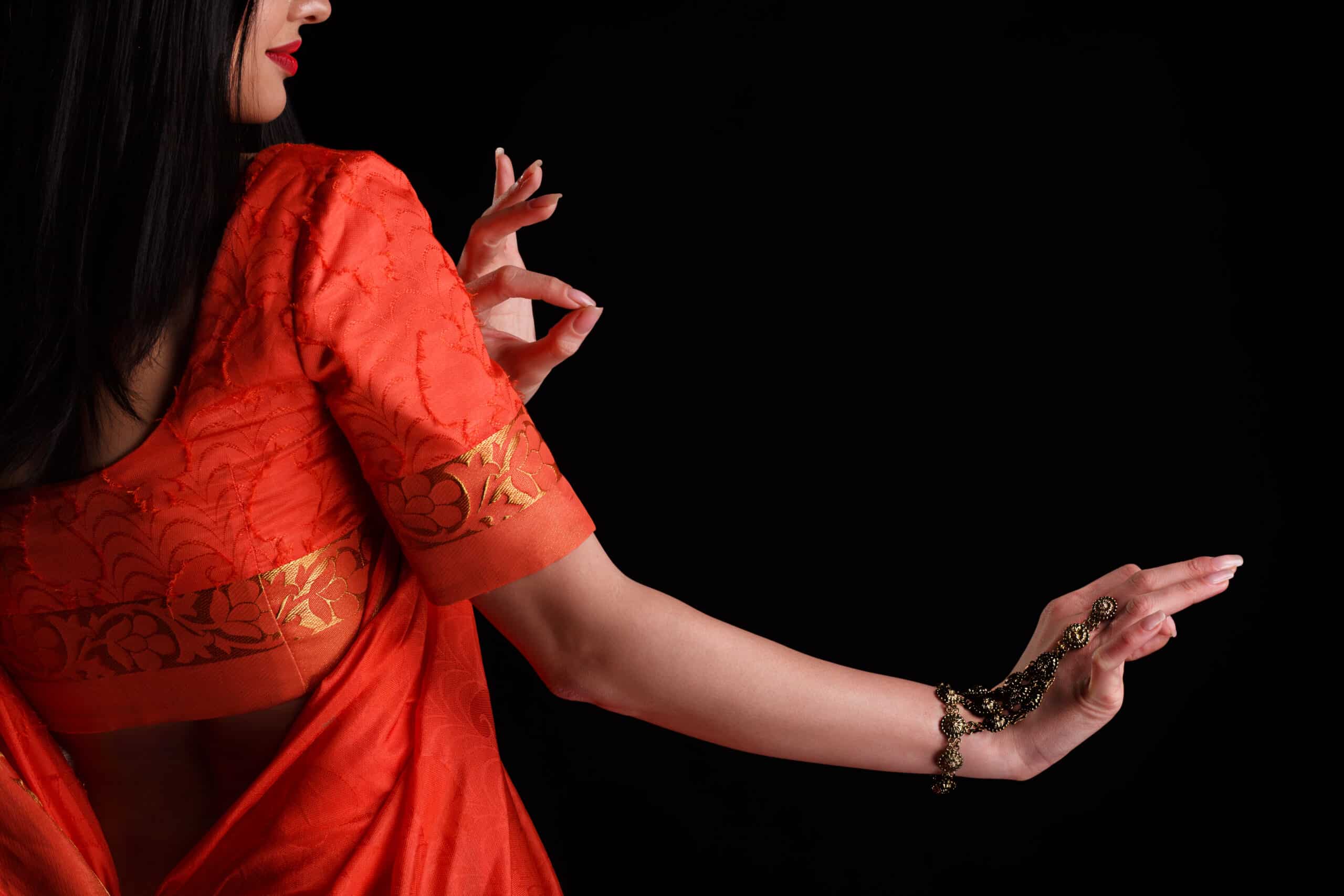 Femme indienne en saree rouge et or, effectuant une danse traditionnelle avec des mudras élégants et un ornement de main.